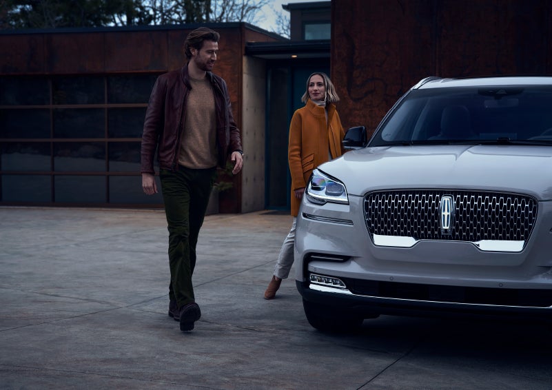 A man and a woman approaching a 2024 Lincoln Aviator® SUV, which illuminates certain lights when they are close | Lincoln of Cutler Bay in Miami FL