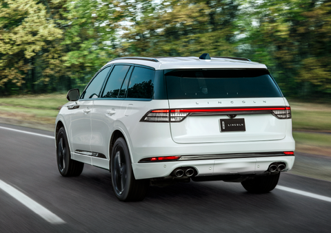 A white 2025 Lincoln Aviator® SUV is being driven away down a road lined with colorful trees. | Lincoln of Cutler Bay in Miami FL