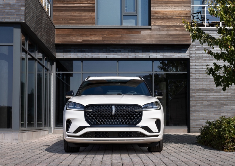 A white 2025 Lincoln Aviator® SUV is shown parked outside a modern building with gray brick and wood accents. | Lincoln of Cutler Bay in Miami FL