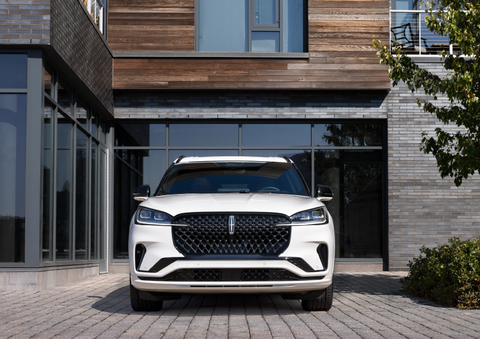 A white 2025 Lincoln Aviator® SUV is shown parked outside a modern building with gray brick and wood accents. | Lincoln of Cutler Bay in Miami FL