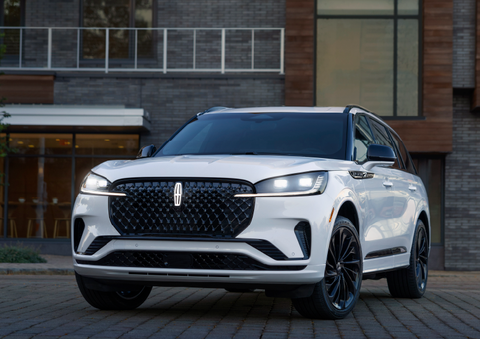 A white 2025 Lincoln Aviator® SUV is shown parked outside a modern building with gray brick and wood accents. | Lincoln of Cutler Bay in Miami FL