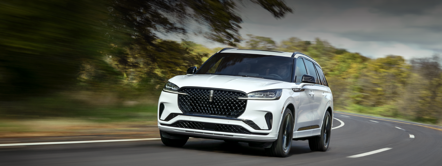 A white 2025 Lincoln Aviator® SUV is being driven down a road lined with trees. | Lincoln of Cutler Bay in Miami FL